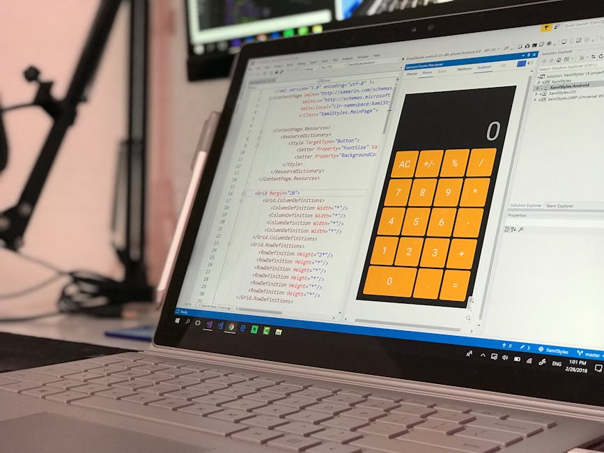 A close-up view of a laptop displaying a software development environment with code on the left side of the screen and a large, orange calculator interface with black buttons on the right side. The la